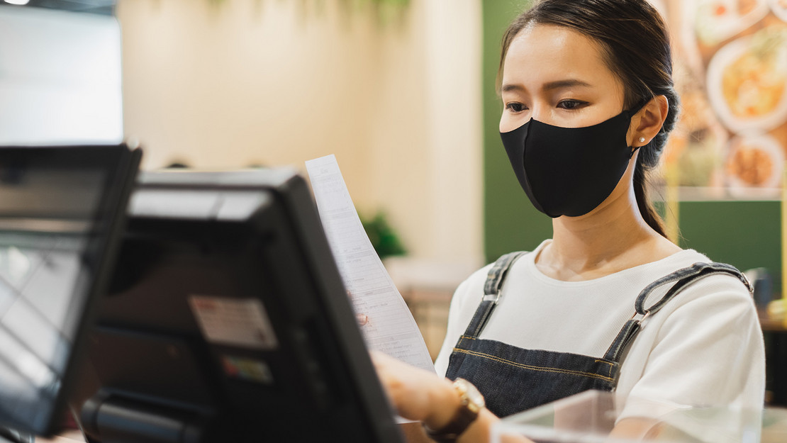 Frau mit Maske arbeitet an einem Kassenterminal