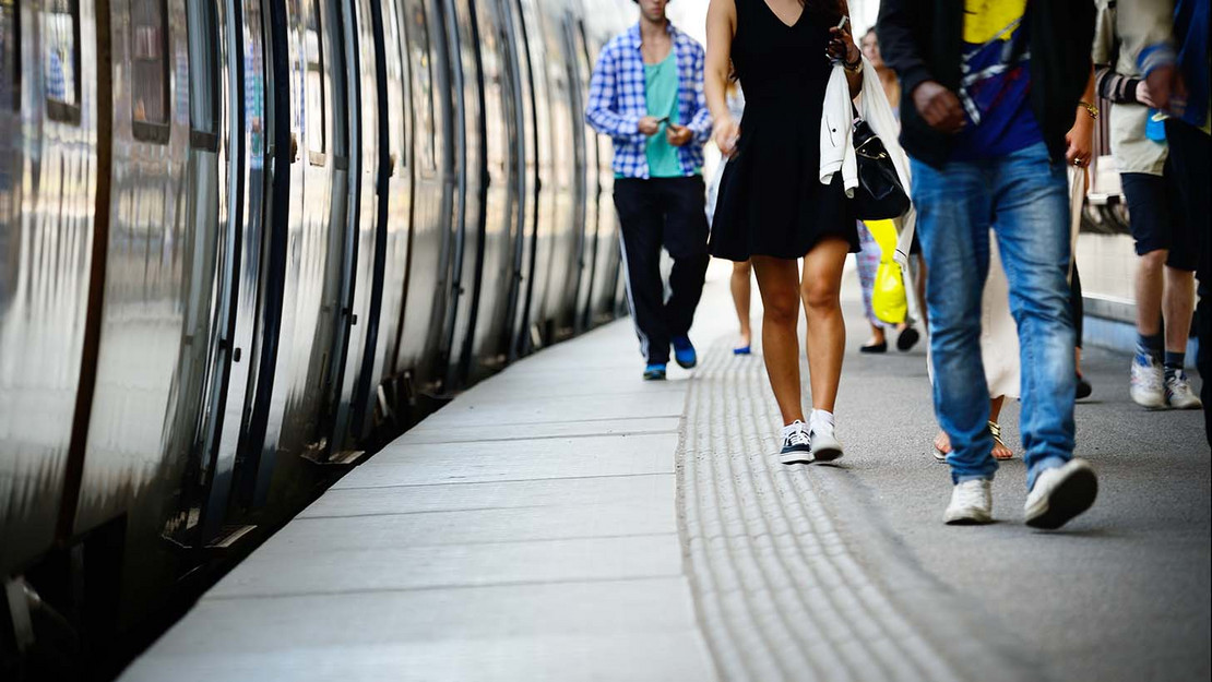 Zug steht am Gleis, Menschen laufen auf dem Bahnsteig. 